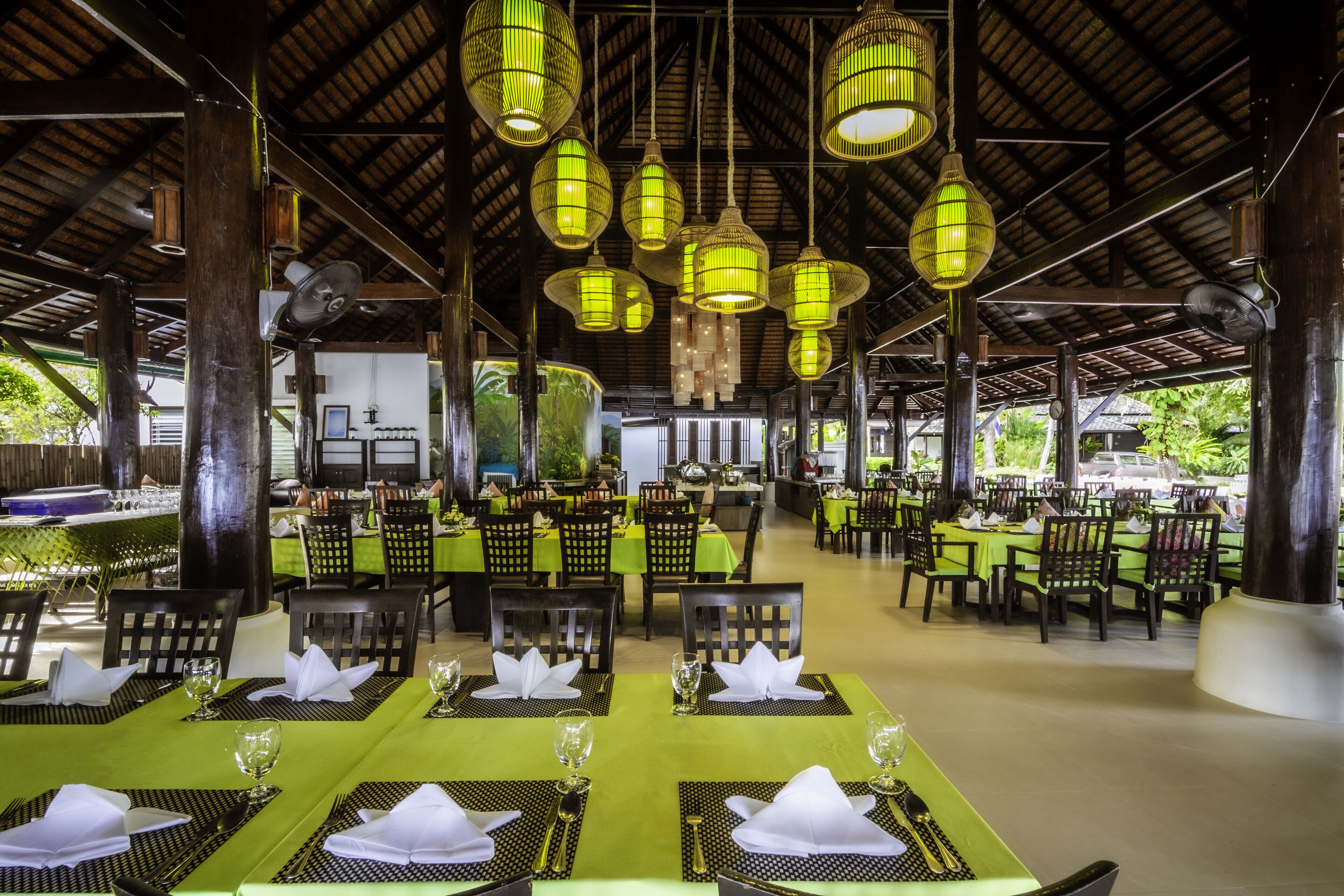 A restaurant with tables set for dining, hanging green lanterns, and a view of the outdoors.