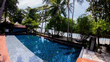A swimming pool with a tiled deck, surrounded by palm trees and a view of the sea.