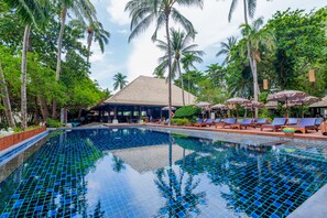 Relax by the serene pool surrounded by lush greenery and palm trees.