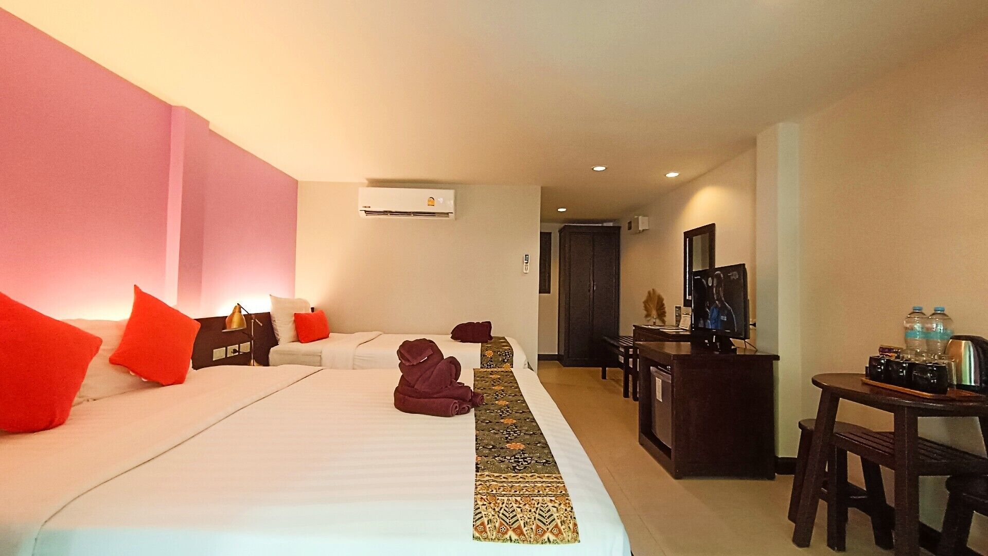 A hotel room with a large bed, a desk, a TV, and a minibar.