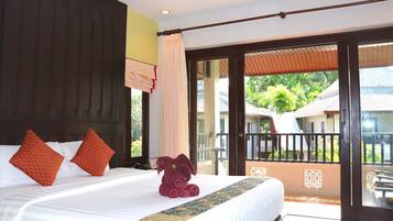 A hotel room with a large bed, two red pillows, a rolled towel, and a view of the outside balcony.