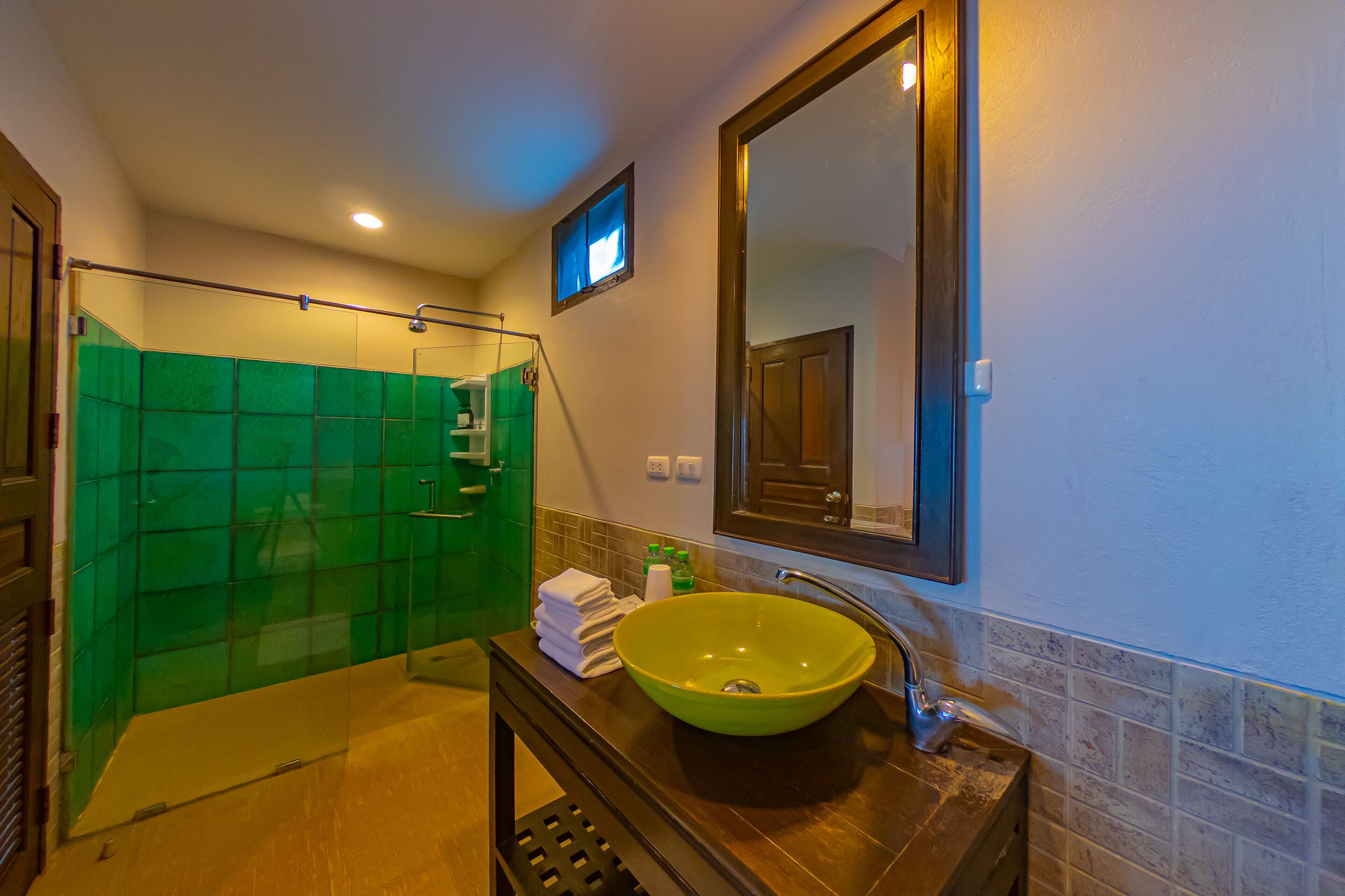 Un baño con ducha de azulejos verdes, un lavabo con cuenca verde y un espejo sobre el lavabo.