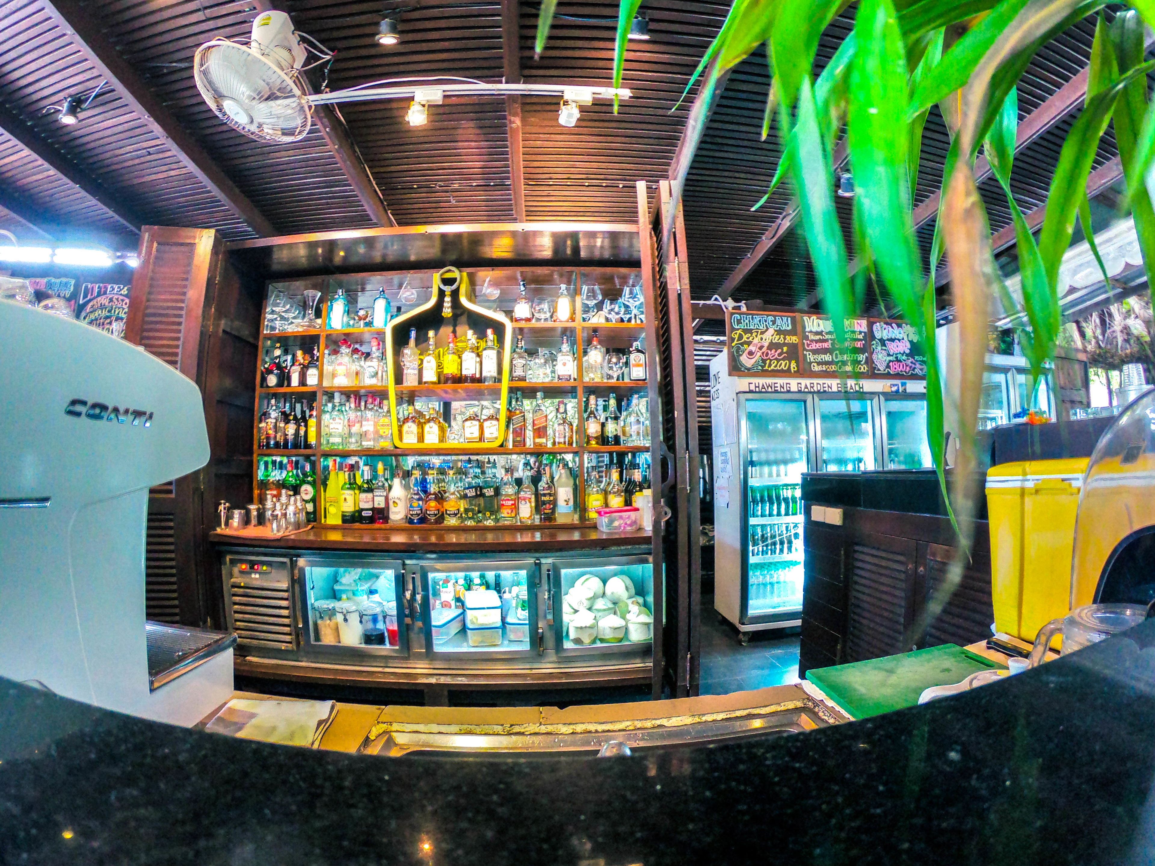 A bar area with shelves of liquor bottles, a refrigerator, and a counter.