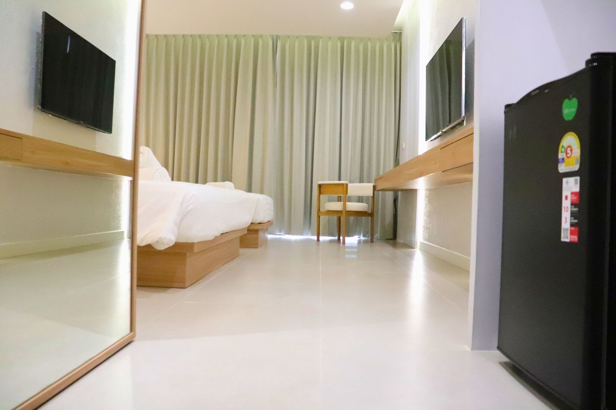 A hotel room with a bed, a chair, a television, and a refrigerator.