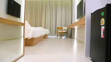A hotel room with a bed, a chair, a television, and a refrigerator.