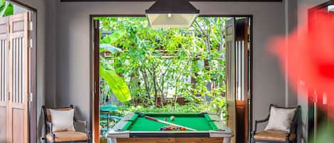 A pool table with a green felt surface, surrounded by two wooden chairs with cushions.