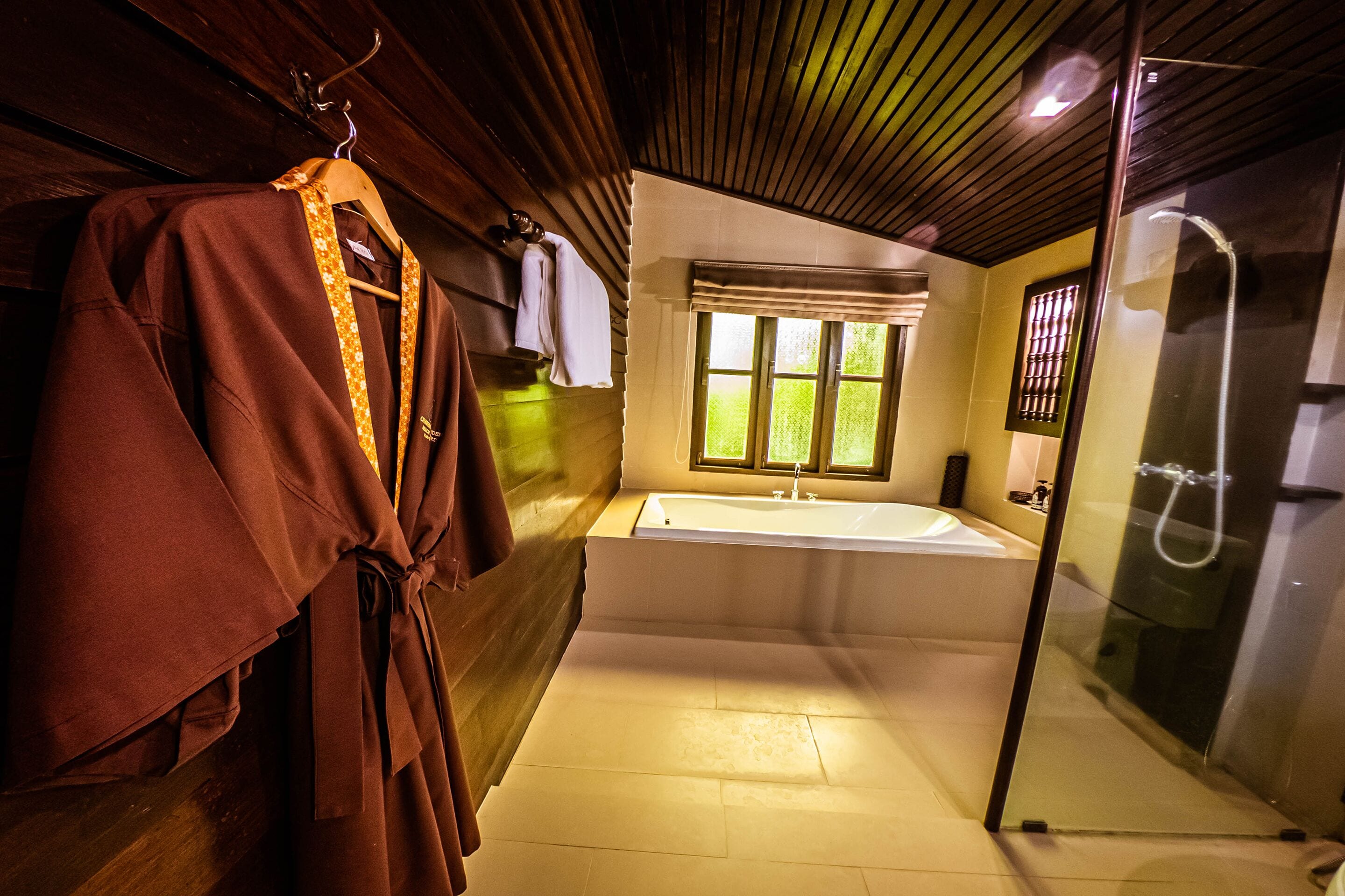A bathroom with a bathtub, a glass shower enclosure, and a wooden wall.
