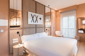 Una habitación de hotel moderna con una cama grande, mesitas de noche, una pequeña zona de estar y un ventanal con vistas.