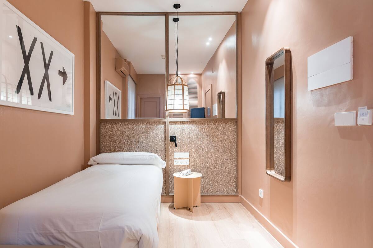 A hotel room with a bed, a round table with a phone, a mirror, and wall-mounted artwork.