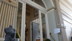 A grand staircase with ornate columns and a chandelier, leading to an interior space with a refrigerator and a potted plant. - Hotel Asiris (Bruges)