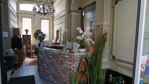 A reception area with a brick counter, potted plants, a chandelier, and a large window. - Hotel Asiris (Bruges)