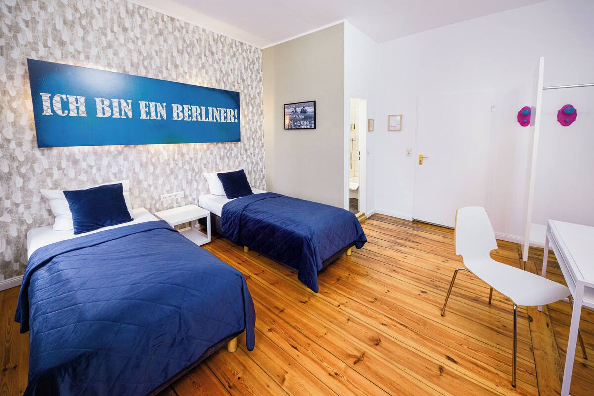 Ein Hotelzimmer mit zwei Betten, einem Schreibtisch, einem Stuhl und einem großen, blauen Schild an der Wand.
