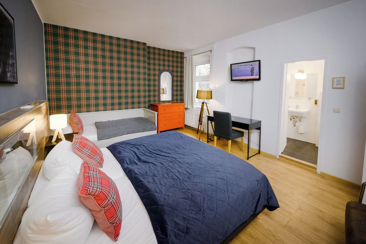 Ein Schlafzimmer mit Bett, Kommode, Schreibtisch und Fernseher.