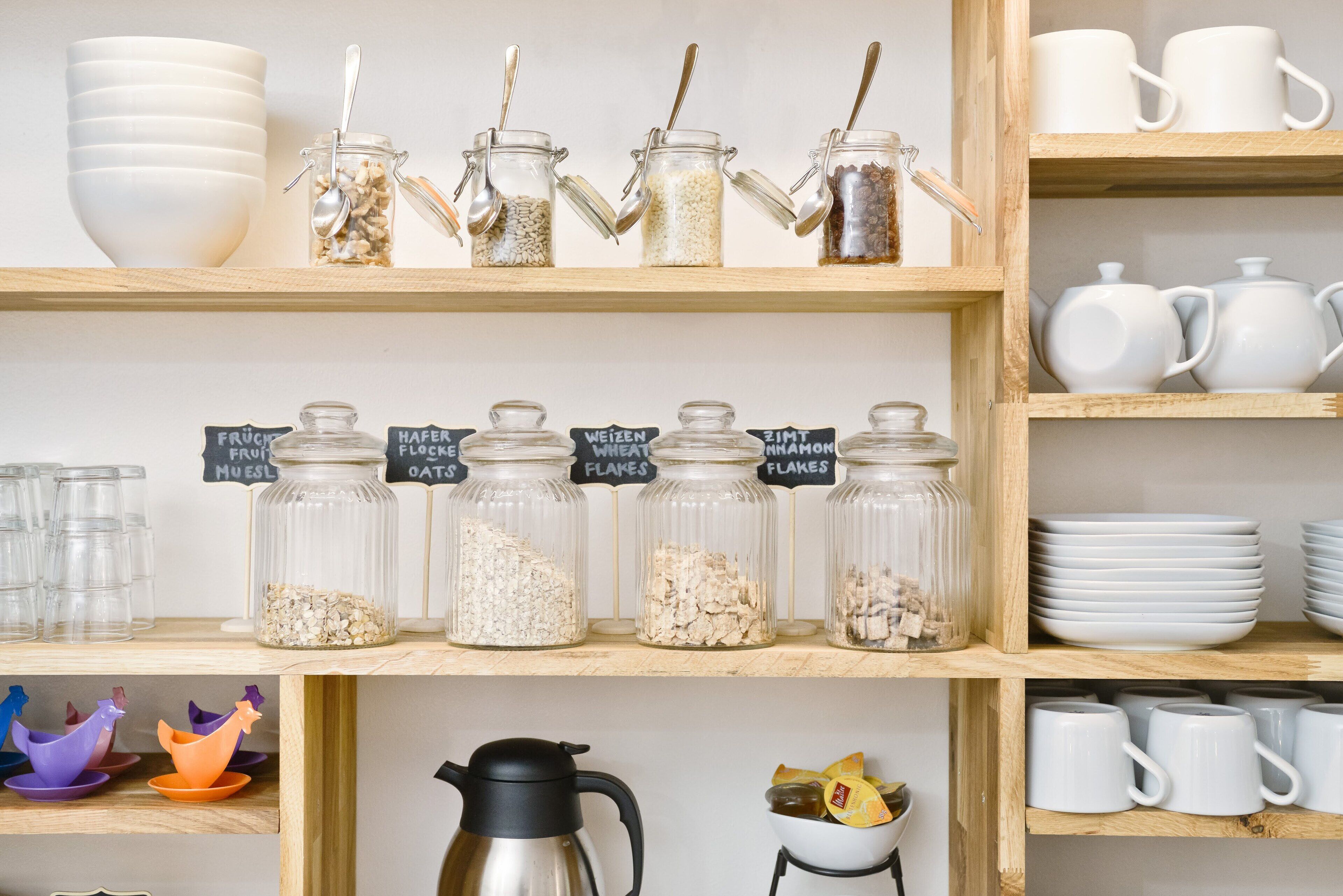 A kitchen shelf with jars labeled with food items like oats and flour, and a coffee maker on a lower shelf.