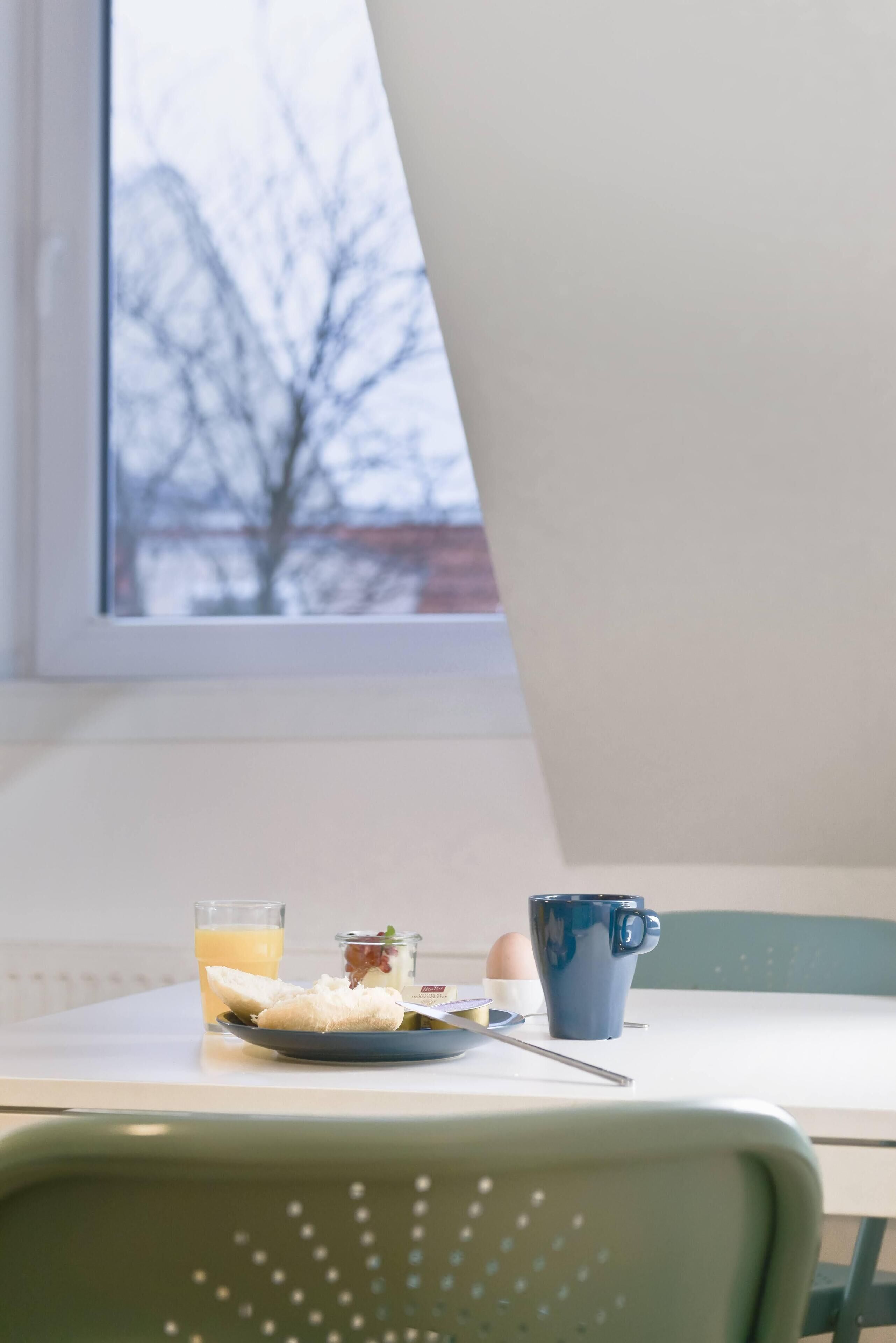 Una mesa de comedor con un plato de comida, un vaso de jugo de naranja y una taza azul.