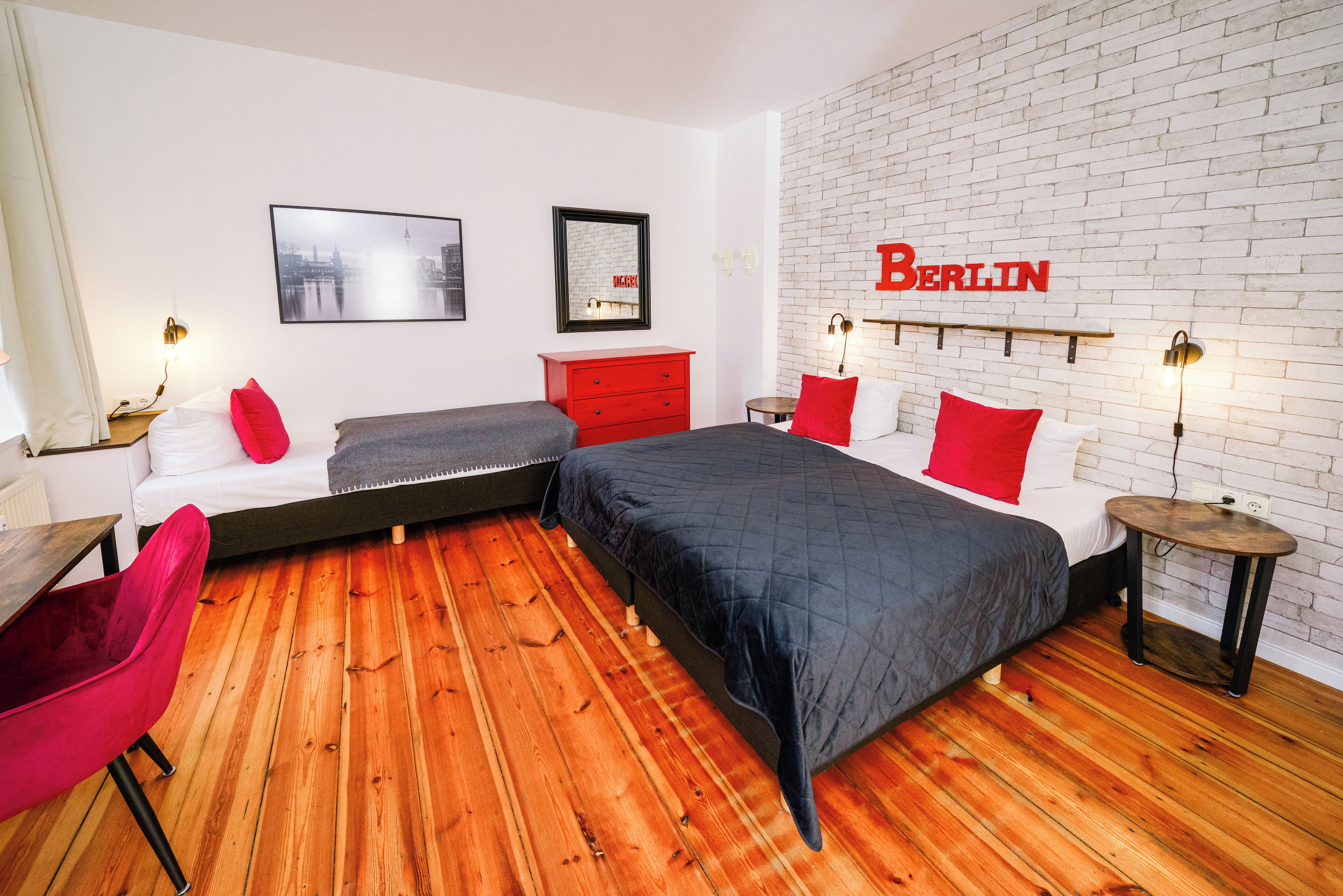 A modern hotel room with a brick wall, a large bed, a red dresser, and a cityscape picture.