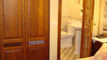A bedroom with a bed, wooden wardrobe, and a bathroom visible through an open door.