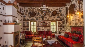 A traditional stone-walled room with a fireplace, wooden furniture, and a red patterned sofa. - Viraggas (Polygyros)