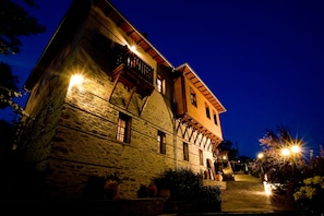 A stone building with a balcony and multiple windows, illuminated by warm lights at night.