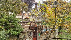 A stone building with a red door, surrounded by greenery and a wooden bridge. - Viraggas (Polygyros)