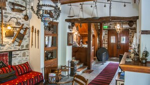 A rustic interior with a stone wall, wooden furniture, a red patterned sofa, and a wooden staircase leading to another room. - Viraggas (Polygyros)