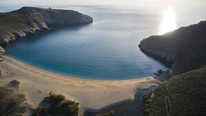 A coastal landscape with a beach, cliffs, and a lighthouse. - Onar Andros (Andros)