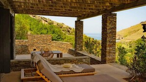 A covered outdoor seating area with stone pillars, a lounge chair, and a view of the landscape. - Onar Andros (Andros)