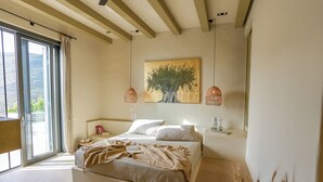 A bedroom with a large bed, a painting of a tree, and two pendant lights. - Onar Andros (Andros)