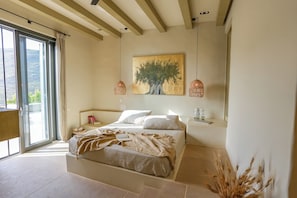 Une chambre avec un grand lit, un tableau représentant un arbre et deux lampes suspendues.