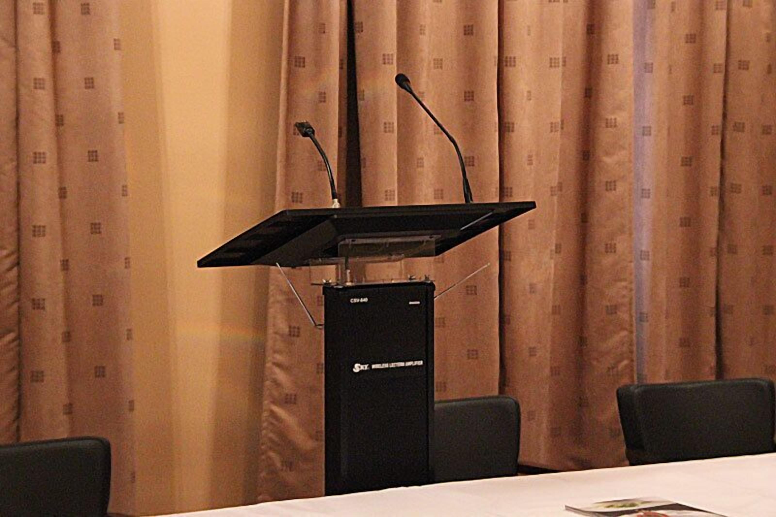 A conference room with a podium, two microphones, and a table with chairs.
