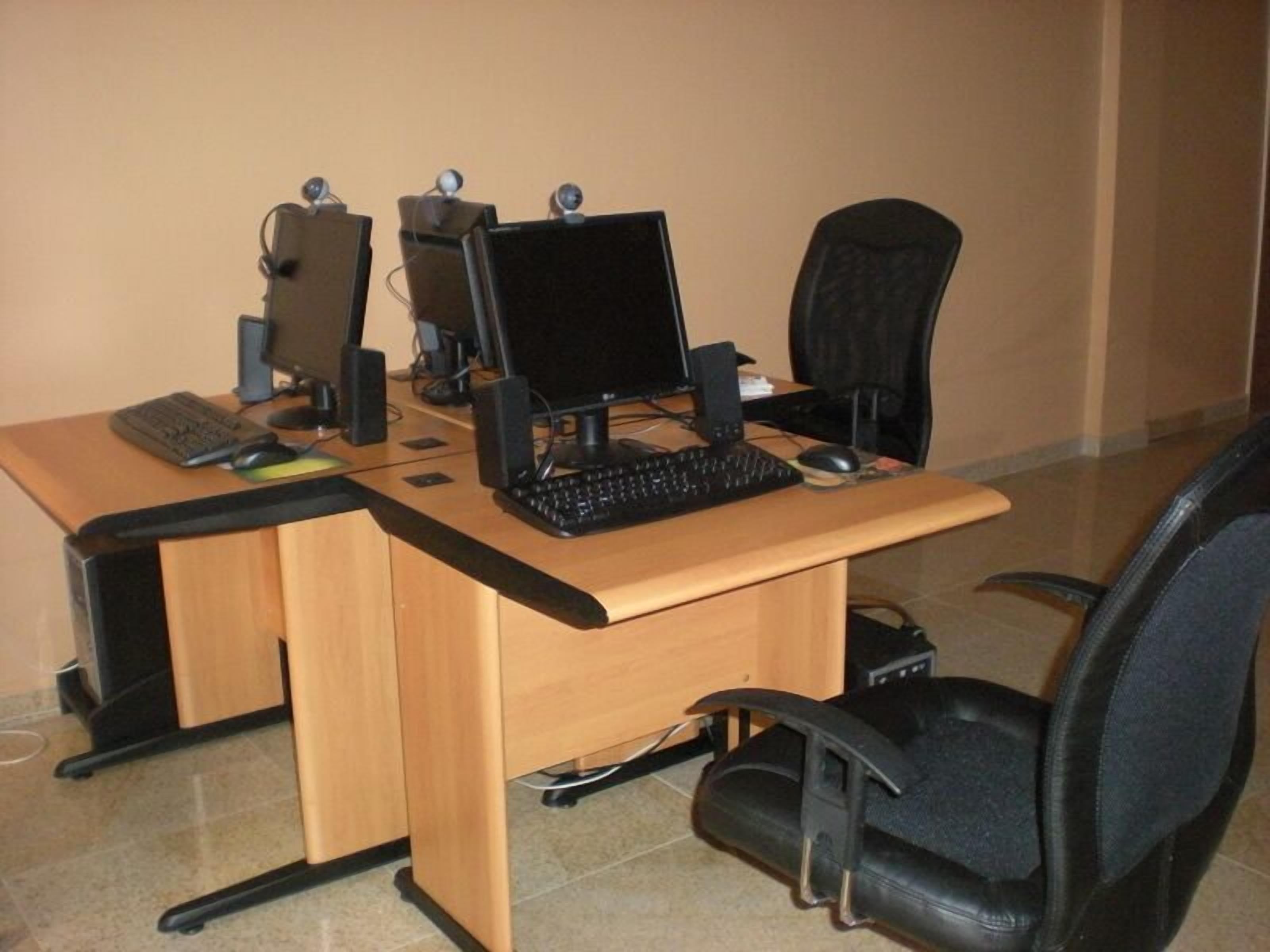 Un escritorio de madera con dos monitores de computadora, un teclado y un ratón. Hay dos sillas de oficina negras.