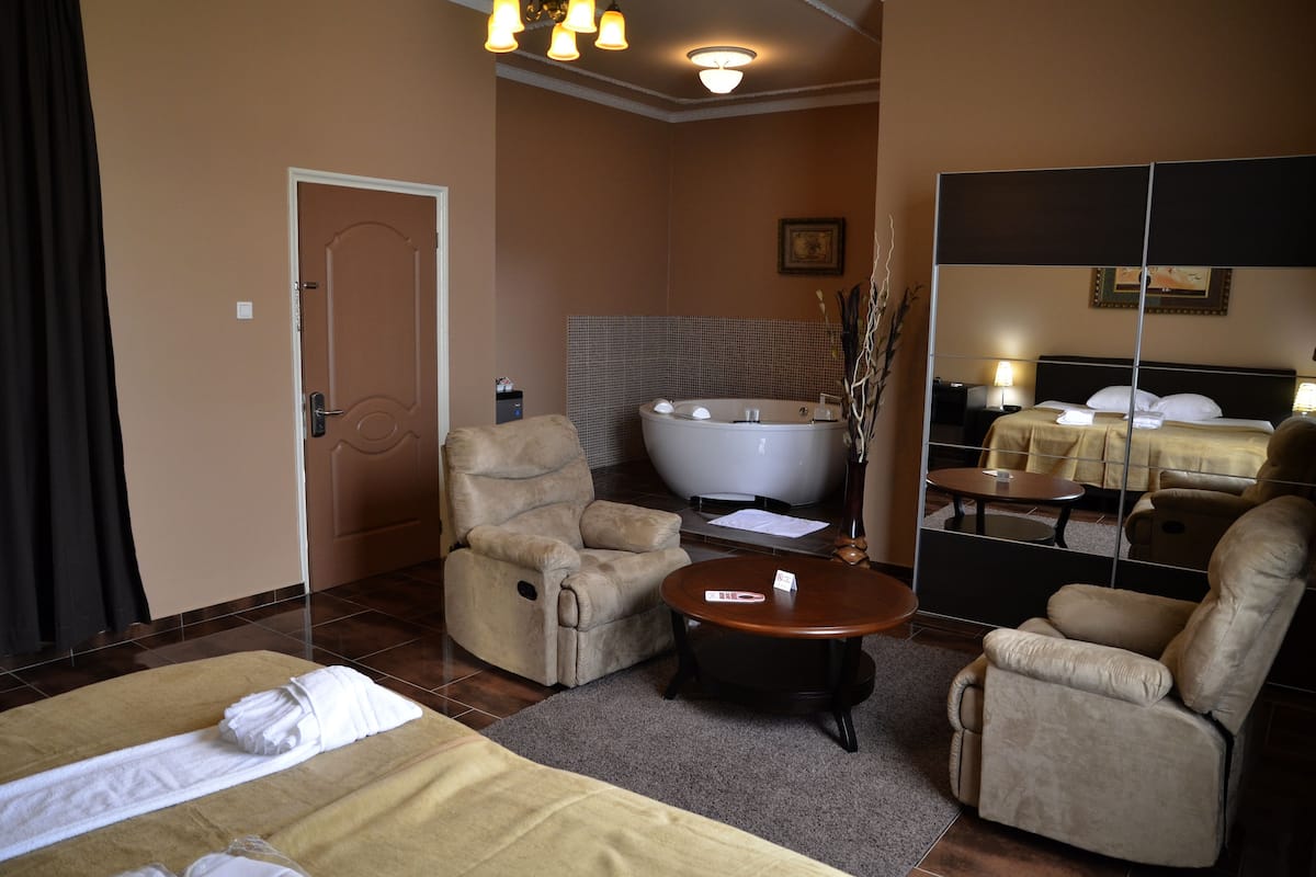 Habitación de hotel con cama, dos sillones, un sofá, una mesita, bañera y espejo.