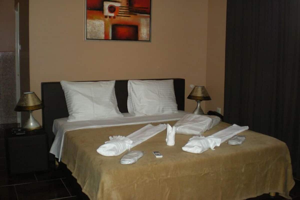 Una habitación de hotel con una cama, dos lámparas de noche, un cuadro en la pared y una cortina.
