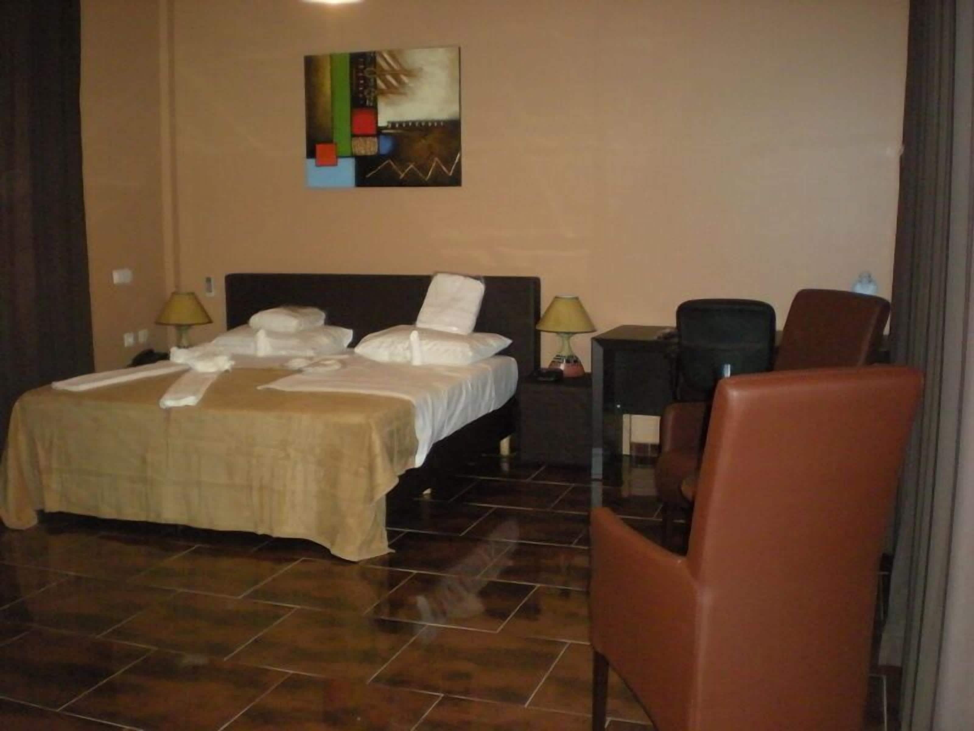 Une chambre d’hôtel avec un lit, deux tables de chevet avec des lampes, une chaise et un tableau au mur.