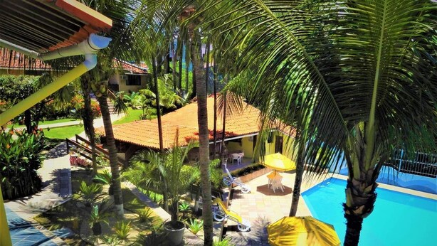 Zona de piscina con palmeras, un deck con baldosas y un edificio con techo rojo.