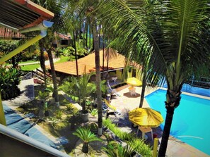 A pool area with palm trees, a tiled deck, and a building with a red roof. - Hotel Tubarao (Natal)