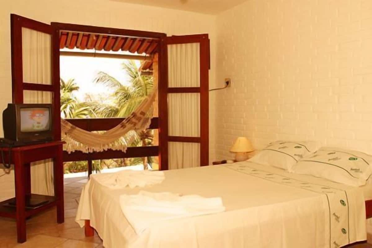 A room with a bed, a television, and a view of palm trees through an open door.