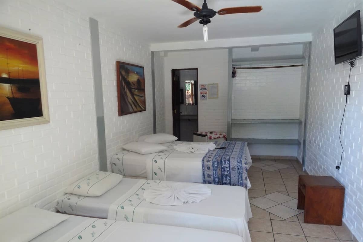 A hotel room with three beds, a ceiling fan, a TV, and a painting on the wall.