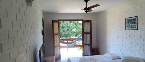 A room with a bed, a ceiling fan, a hammock, and a view of greenery outside.