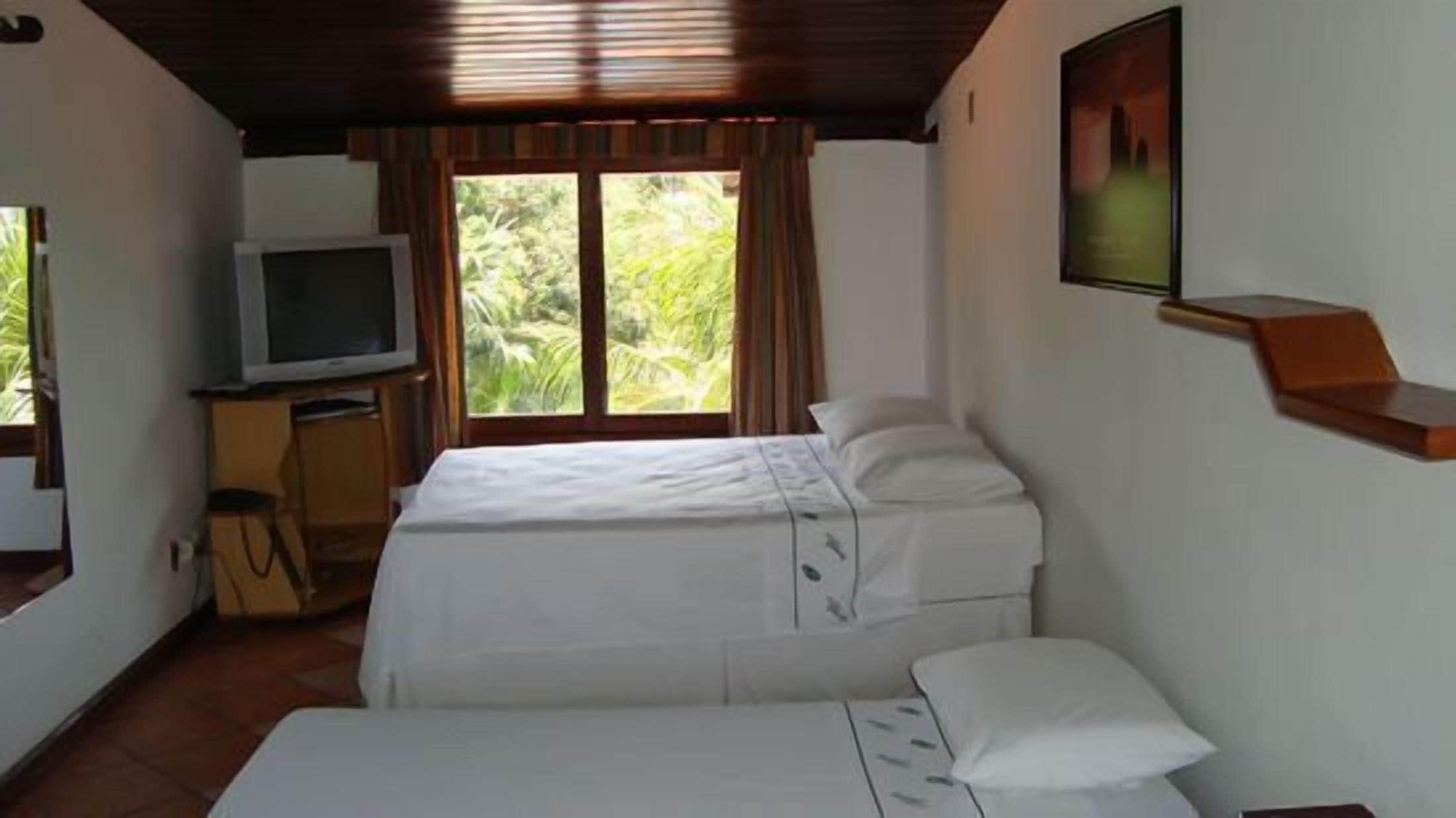 Una habitación con dos camas, televisión y ventana con cortinas.