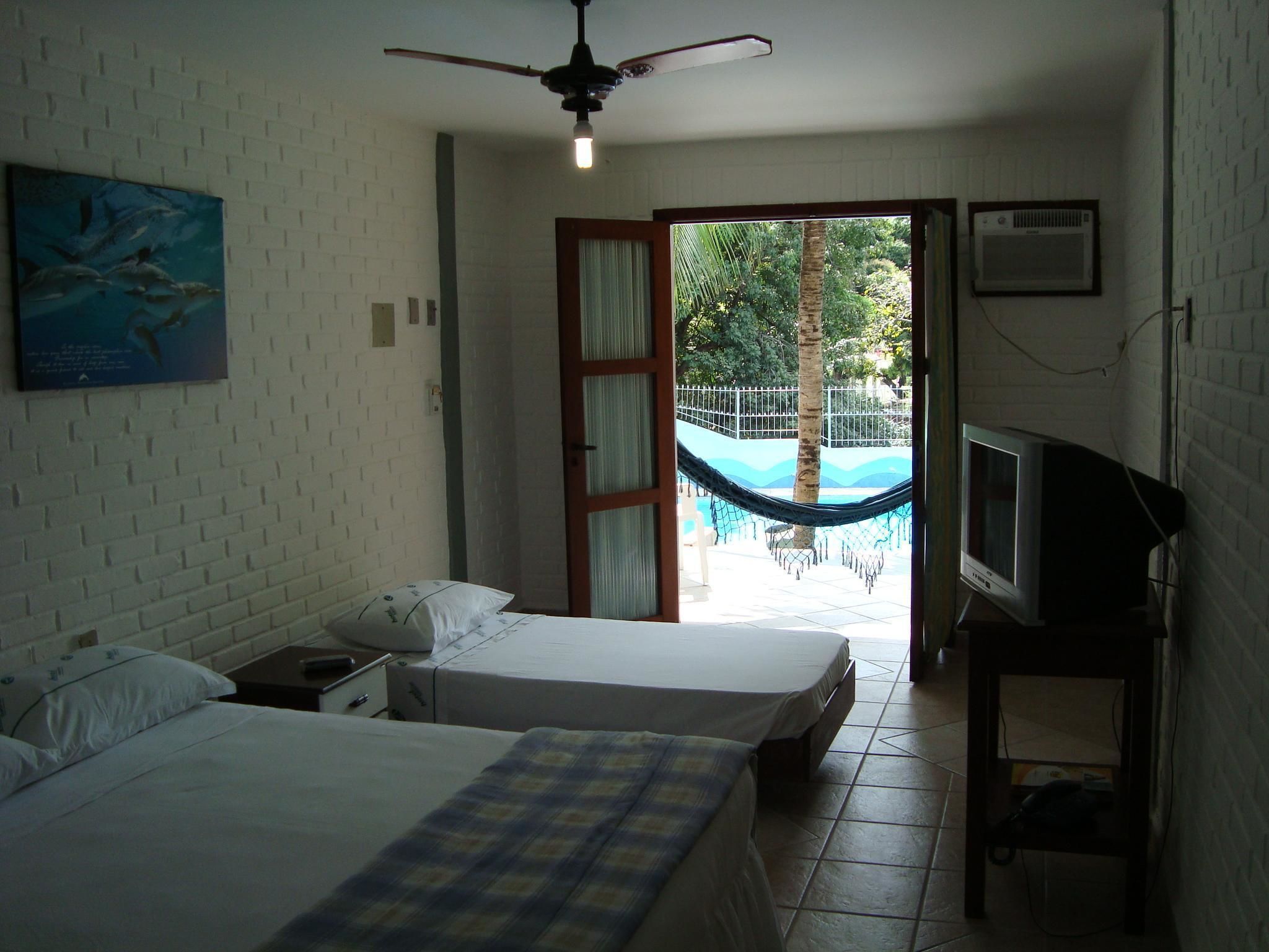 A hotel room with two beds, a television, a ceiling fan, and a view of an outdoor swimming pool.