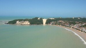 Vista aérea de un pueblo costero con playa, acantilados y cielo despejado.