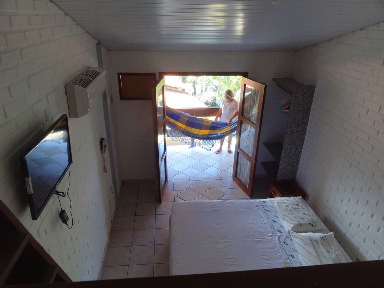 Een kamer met een bed, een aan de muur bevestigde televisie en een hangmat buiten.