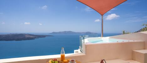 A terrace with a table set for breakfast, overlooking a sea and a mountainous landscape.