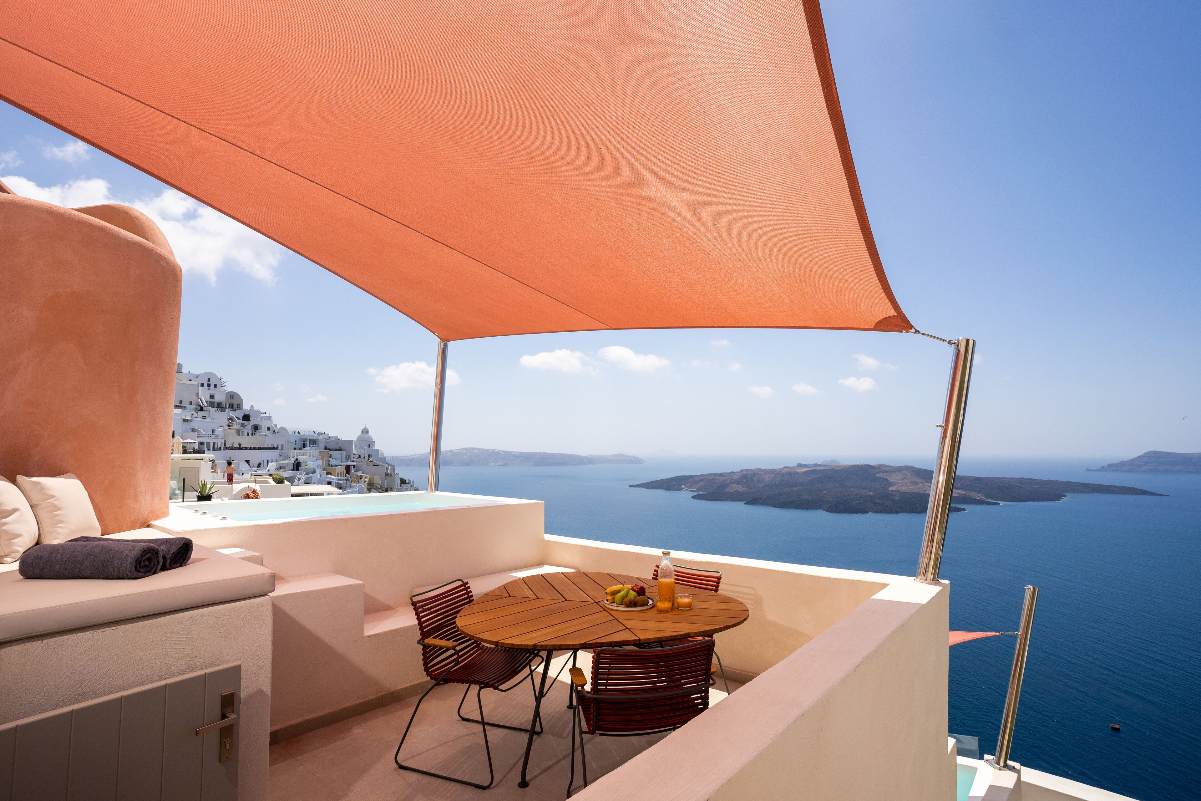 Ein Balkon mit einem Holztisch, Stühlen und einem großen orangefarbenen Baldachin.
