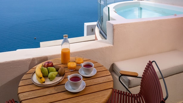 Una mesa con fruta, jugo y té, con vista a una piscina y al mar.