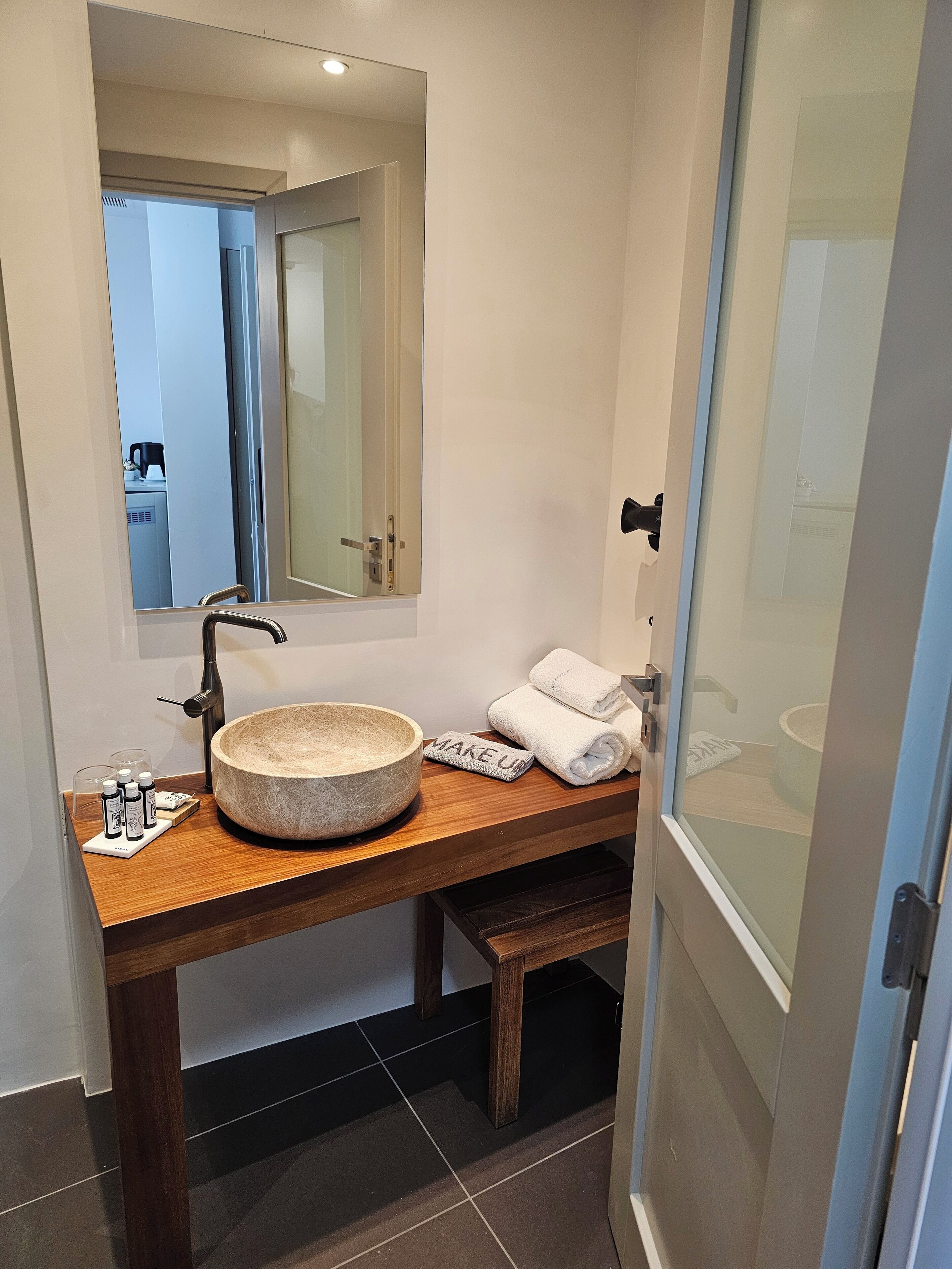 Ein Badezimmer mit einem Holzkosmetikschrank, einem runden Steinsinkenschrank, einem Spiegel und einem Handtuchhalter.