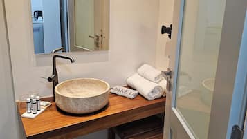 Un baño con tocador de madera, lavabo de piedra redondo, espejo y toallero.