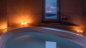 Un baño moderno con una bañera grande, velas y vistas al atardecer a través de una ventana.