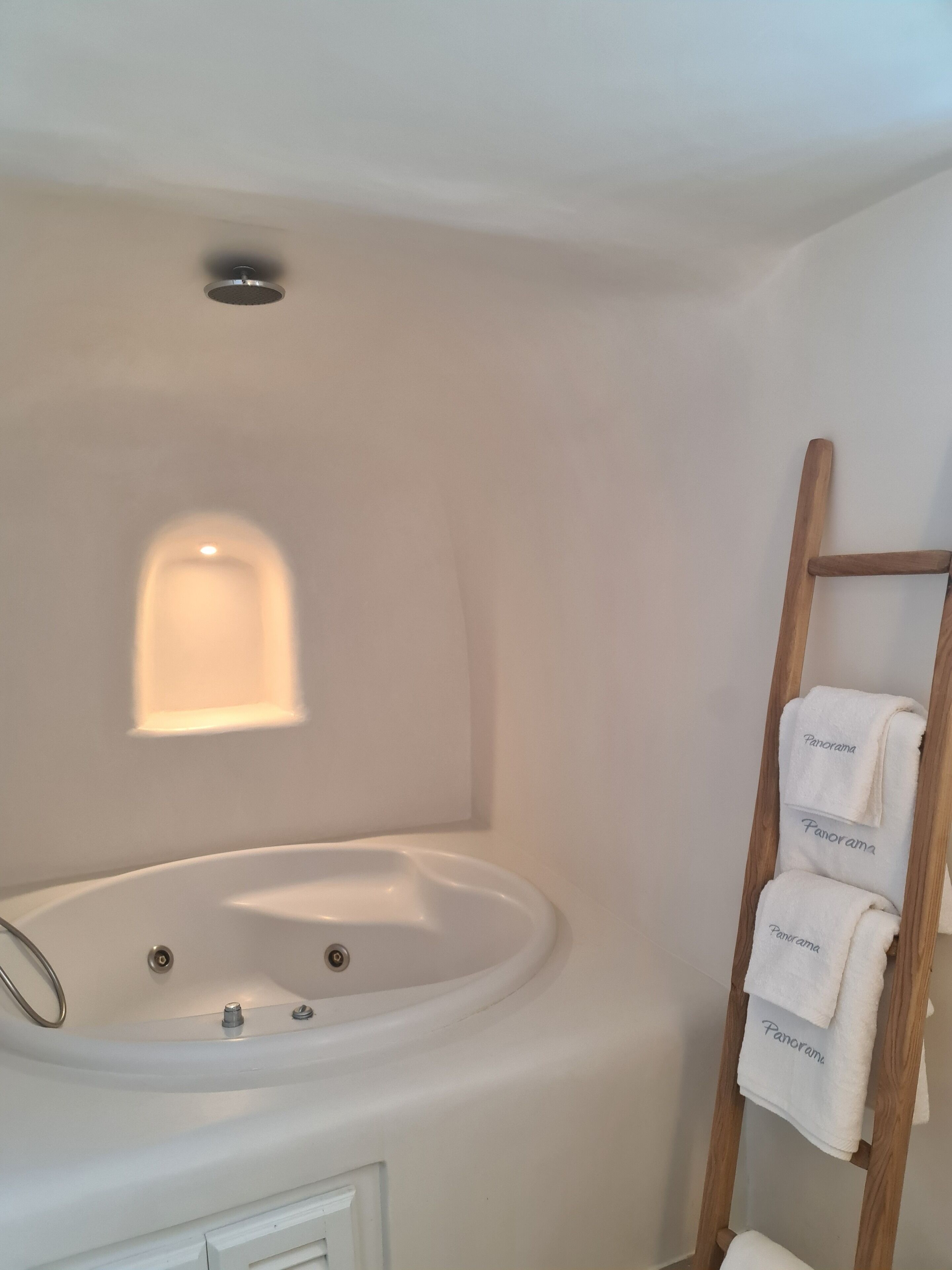 A bathroom with a freestanding bathtub, a wooden towel rack with towels, and a small window.